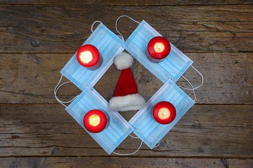 A top view closeup of an advent wreath made of medical masks, burning red candles and a santa hat