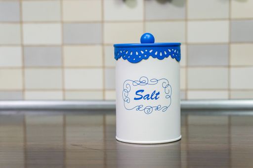 A selective focus shot of a salt container, on a wooden table in the kitchen