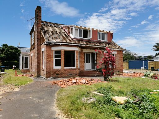 View of old red brick house being demolished with lonely broken blooming decorative tree in front