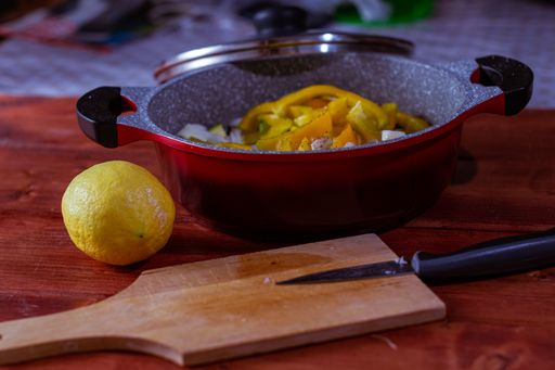 A closeup of a wooden cutting board, a lemon, and a pot filled with seasoned vegetables