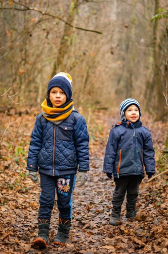 Two young boys standing on a footpath covered with fallen leaves in a forest in the Morasko park on a cold autumn day.