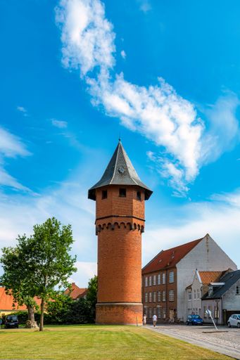 A tall, modern tower standing beside a lush green area beside a road in a sunny day