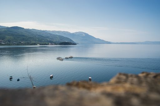 A sea with boats on it surrounded by hills covered in greenery under sunlight