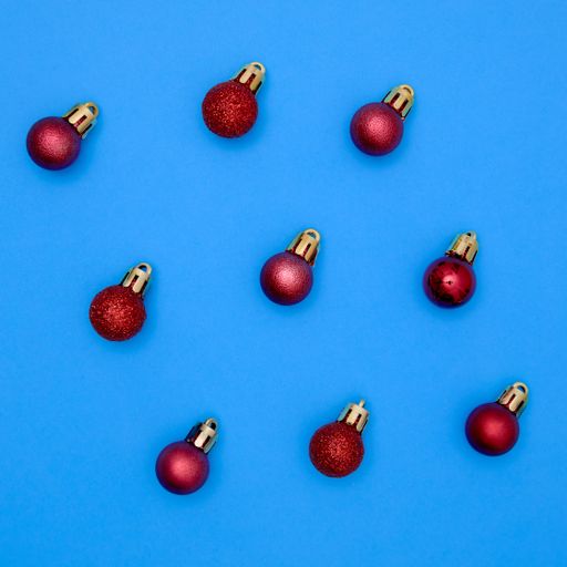 red christmas ball patterns on solid blue background. Balls of different textures and colors, some with glitter.