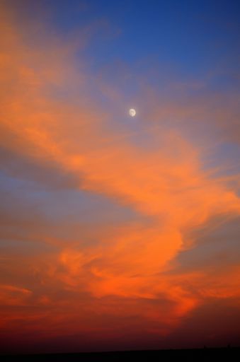 A vertical shot of a tranquil sunset in the sky with the moon