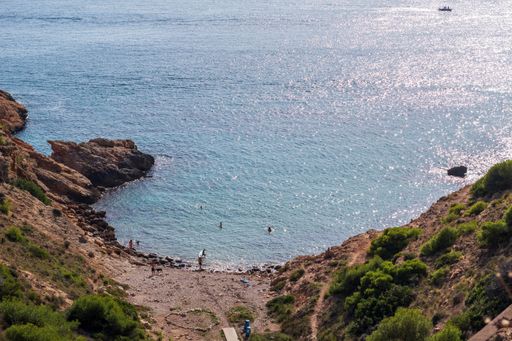 A scenic beach landscape featuring a rocky shoreline stretching out towards the clear blue waters