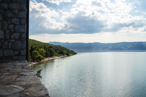 A sea surrounded by greenery and buildings with mountains under a cloudy sky on the background
