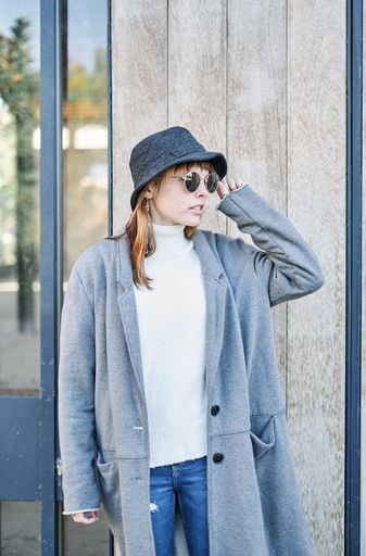 A pretty Caucasian girl dressed in a gray jacket, a white sweater and a hat posing outside