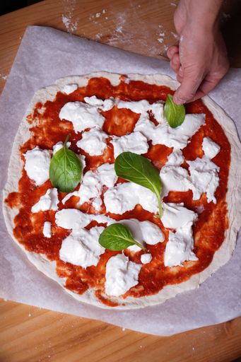 A vertical shot of a cook putting a leaf on the Artisan pizza dough with mozzarella and tomato sauce