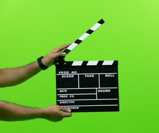 Men's hand holding camera slate for the filming isolated on green background. clapperboard in chroma