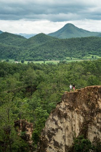 A vertical shot of two guys standing on the edge of the cliff and admiring the amazing natur