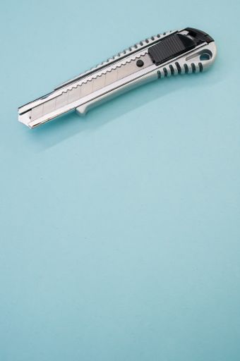 A vertical shot of a cutter blade tool isolated on blue background. Cutting knife for cardboard