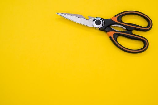 A closeup shot of scissors isolated on yellow background. Cutting tool with zigzag blades, copy space