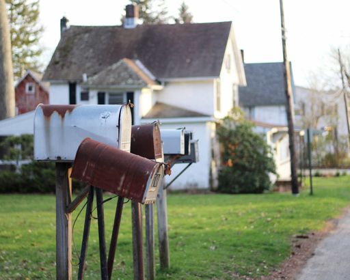 A few mailboxes on posts in the lawn in a residential area with a white house in the background