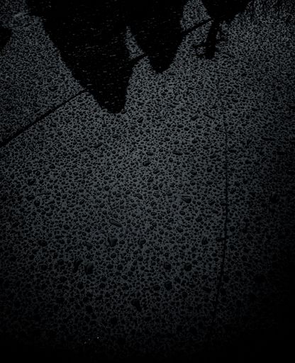 A close-up of raindrops on a car in grayscale
