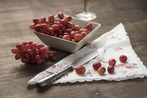 A shot of still life with grape - grape cluster, a bowl of grapes, and grape berries on the embroidered napkin