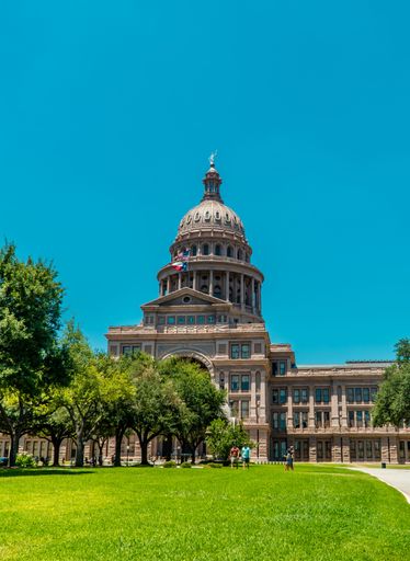 A vertical shot of the Texas State Capitol under blue sky on a sunny day in downtown Austin, Texas