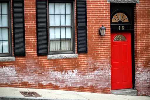 A red entrance door to a brick building showing number sixteen on a street with glass windows