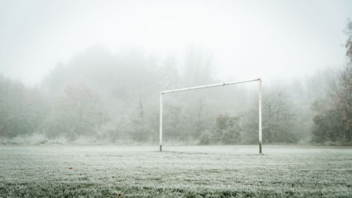 A soccer goal stands in the middle of a misty field on a gloomy day