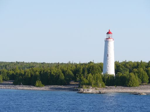 A shot of a lighthouse near the water under the clear sky
