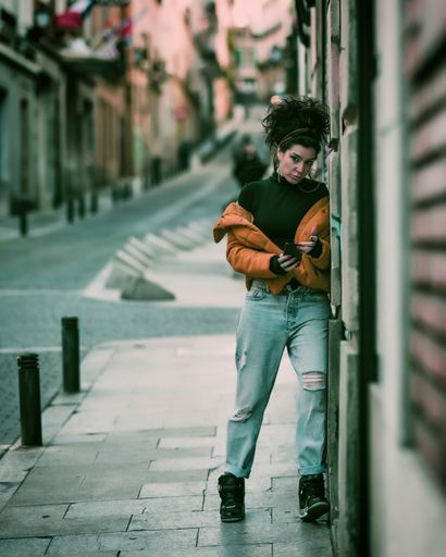 A vertical shot of a woman checking her surroundings while using her phone outdoors