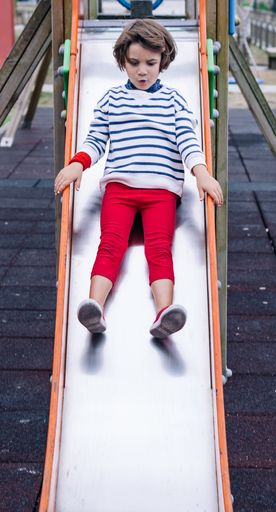 The picture shows a little girl going down a slide in a playground