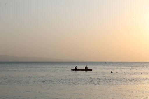 A beautiful sceneryof a small boat with two sailors in the sea during the sunset