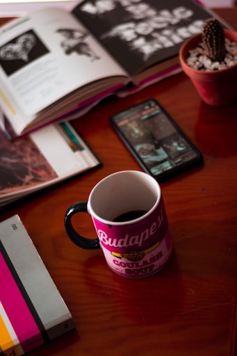 A vertical shot of a mug on the desk with a book and open smartphone, pot with cactus