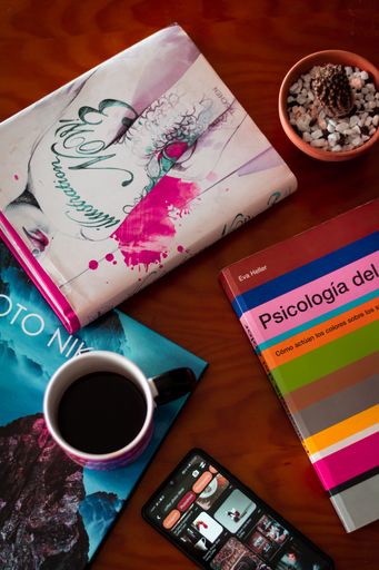A vertical shot of a mug on the desk with a book and open smartphone, pot with cactus