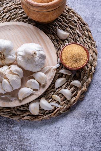 A vertical shot of minced garlic in a bowl with white garlic on the side