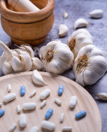 A closeup of pills on a wooden plate and garlic on the si