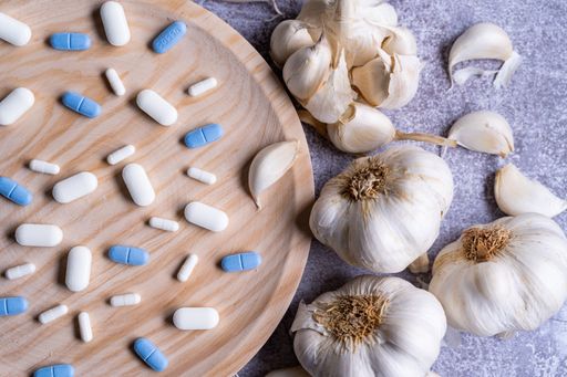 A closeup of pills on a wooden plate and garlic on the side