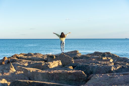 A female with open arms standing on rocky beach in Benicasim, Spain