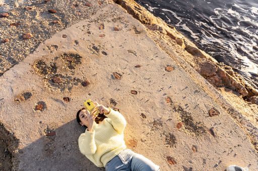 A top view of a Caucasian brunette using a her phone while lying on a beach in Benicasim, Spain