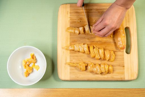 A top view of a person cutting a chicken breast on a wooden board