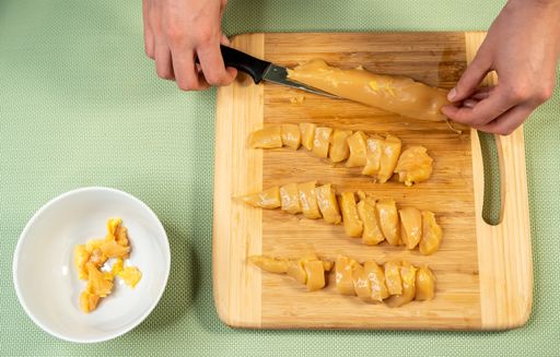 A top view shot of a cook cutting chicken fillet on a cutting board