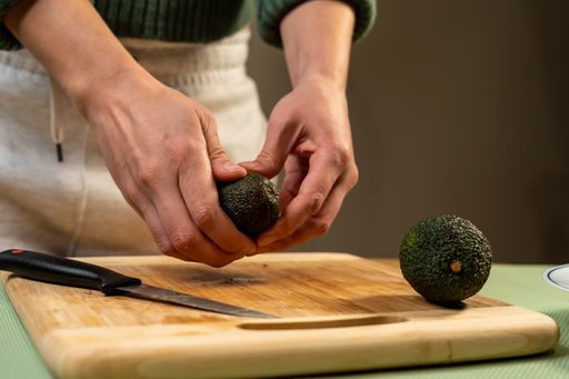 A selective focus shot of a cook cutting avocado on a cutting board for sushi