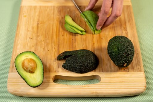 A selective focus shot of a cook cutting avocado on a cutting board for sushi