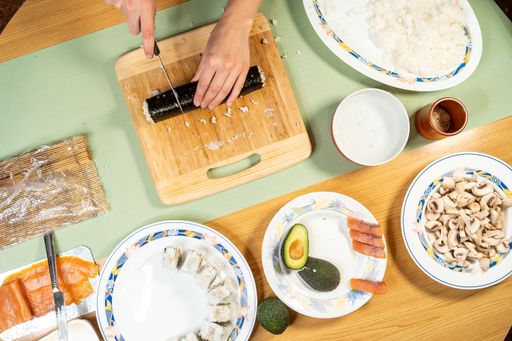 A top view shot of a cook cutting sushi on a cutting board and various ingredients on table