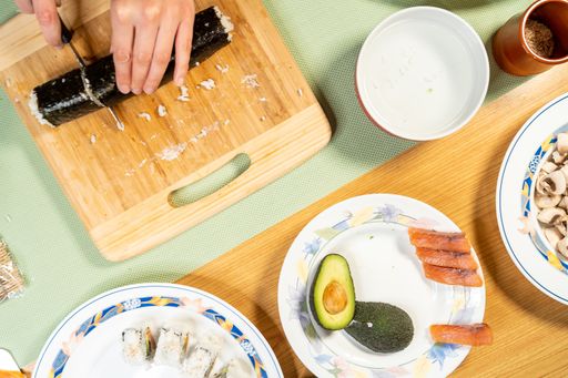 A top view of a person cutting sushi rolls on a wooden board on the table