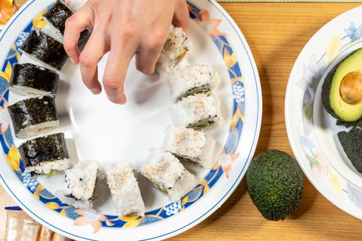 A top view of a person putting California rolls with avocados and fish on a plate on the table
