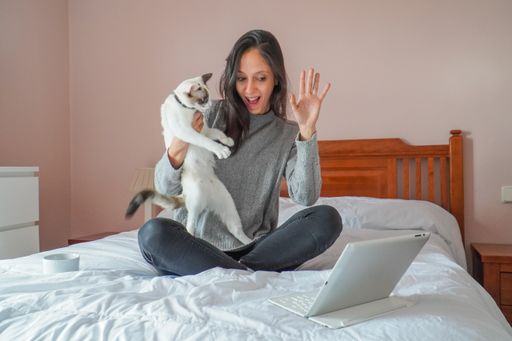 Young caucasian woman making a videoconference with her cat, siting on bed with a casual style