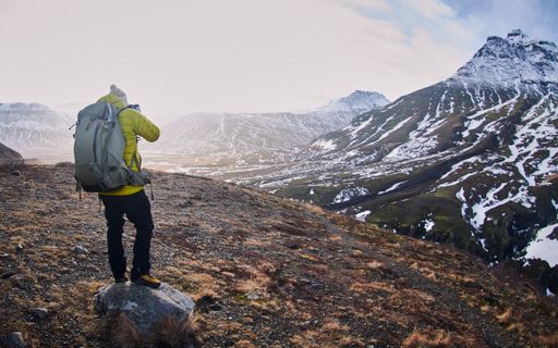 A male wearing a yellow jacket and a backpack while taking a picture of the beautiful scenery