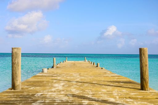 A wooden pier extending out into a tranquil and inviting turquoise ocean, situated at the end of a sandy beach