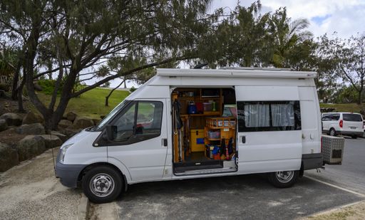 A white compact van with household goods in it in a park surrounded by greenery