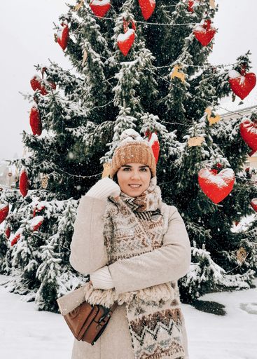 A vertical shot of a smiling Caucasian female standing in front of a Christmas tree