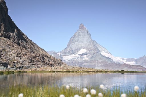 The majestic Matterhorn stands tall behind a tranquil lake against the backdrop of blue sky.