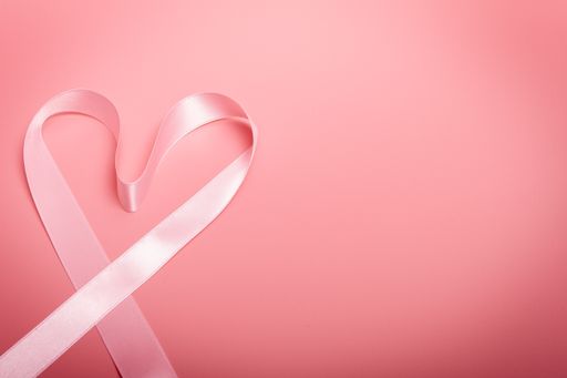 A heart-shaped pink tape on a pink background-symbol of awareness and fight against breast cancer