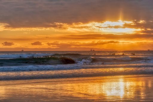 A beach surrounded by the wavy sea under a cloudy sky during a golden sunset