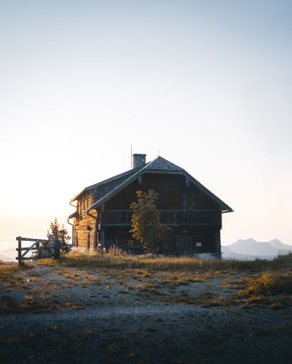 A vertical shot of a small wooden house in an open meadow under the sky